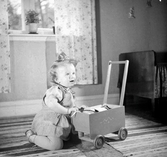 En liten flicka leker med en dockvagn av trä.
