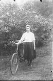 Ungdomsporträtt, kvinnoporträtt av en ung kvinna med cykel. Hon är klädd i kjol och blus.