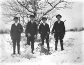 Gruppbild av ett jaktlag med hundar. Tre av männen har gevär. Vinterbild med snö.