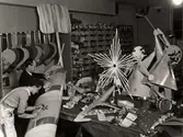 Jularbete på dekorationsavdelningen, Nordiska Kompaniet 1939. I ateljén, där två män arbetar, ligger julprydnader.