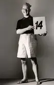 Nordiska Kompaniets kabaré april 1943. Man iförd shorts, kortärmad sportskjorta, sandaler och mössa med tofs. Han håller upp en skylt med talet 14.