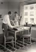 Interiör från kök där man och kvinna monterar ihop köksmöbler ur NK:s, Nordiska kompaniet, TRIVA-serie.