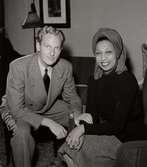 Monsieur Erik och sångerskan Josephine Baker sitter tillsammans i en möblerad interiör på varuhuset Nordiska Kompaniet i Stockholm i mars 1946.