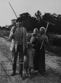Lantarbetarfamilj. Gotthard Fredrik Fredriksson och Edla Fredriksson med två barn. På landsväg med lie och räfsa. Danderyd, Uppland.