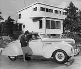 Kvinna i samtal med en passagerare i en vit Plymouth 1939, cabriolet. Nordiska Kompaniet.