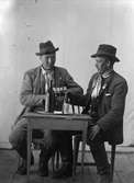 Ateljéporträtt av två unga män vid bord med ölflaskor