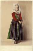Kvinna i helfigur klädd i högtidsdräkt för gift kvinna från Vemmenhögs härad, Skåne. Handkolorerat fotografi