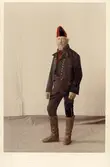 Man i helfigur klädd i festdräkt från Bjuråkers socken, Hälsingland. Handkolorerat fotografi