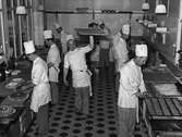 Interiör från köket på konditoriet i Nordiska Kompaniet. En grupp bagare i arbete. Några dekorerar tårtor, andra skär bröd på plåtar. 7 maj 1947.