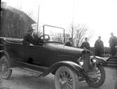 En man sitter i en bil invid järnväg. Fyra uniformsklädda män i bakgrunden.1920-1922.Overland 4cyl.