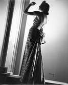 Modell i balklänning med silverfärgade ränder, klädda knappar i ryggen och stor rosett baktill.