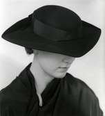 Kvinnlig modell i hatt från Rose Valois. Svart filt med ripsband. Nordiska Kompaniet, Stockholm.