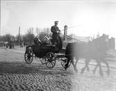 Manliga studenter åker häst och vagn med uniformsklädd kusk på Östra Ågatan, Uppsala