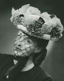 Porträtt av kvinna i hatt med dekorband, garneringar och flor, av Monsieur Erik.