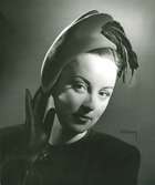 Porträtt av kvinna med hatt i röd filt med svart fjäder. Uppvisning mars 1947. Hattar använda vid franska avdelningen.