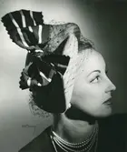 Porträtt av kvinna med hatt i rosa filt med vitt och marinblått band. Uppvisning mars 1947. Hattar använda vid franska avdelningen.