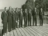 Grupporträtt av män i olympisk dräkt på en kaj.