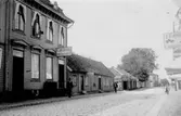 Östra Långgatan mot norr, kv Apotekaren 9. Husen till vänster ligger i kvarteret Apotekaren. På skyltarna görs reklam för: Café Berlin -vin öl och porter, Stuf och kommisionsaffär Albertina Carlsson, Förgät mig ej, C O andersson toffelmakeri. 1910-tal