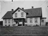 Exteriör av fattighuset Nyhem i Drängsered. Ett stort trähus på stenfot med stora spröjsade fönster och veranda med figursågat räcke, där tre personer står, troligen ur personalen.