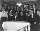 Grupporträtt av ungdomar inomhus vid ett bord med en tänd fotogenlampa.