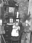 Porträtt av en liten flicka som står på en stol, inomhus.