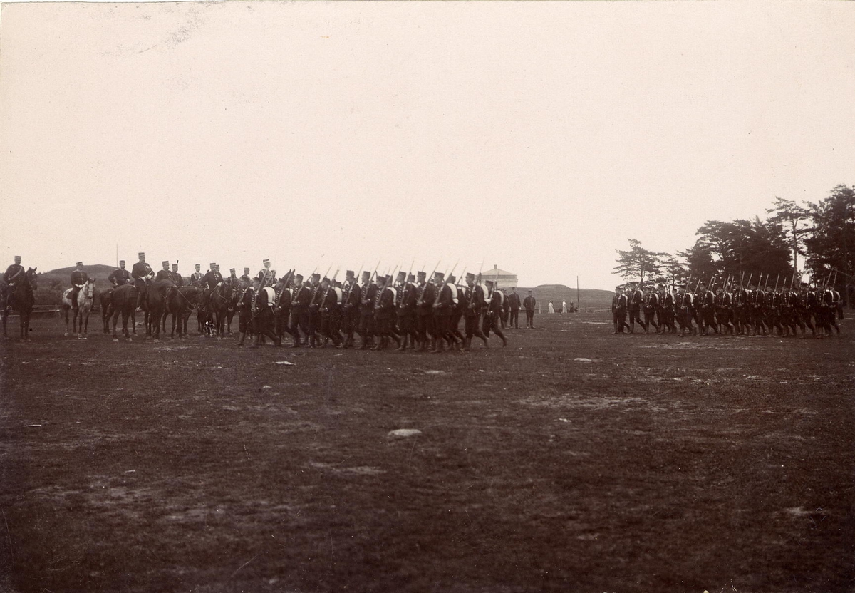 Axel Sjöberg & Co, Soldiers on foot marching pre-car officers to horse. In the background, Karlsborg Fortress is glimpsed. Female spectators look at the background, Karlsborg 1902.