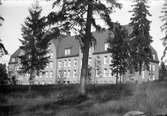 En stor tegelbyggnad med tegeltak, i förgrunden barrträd. Det är  Lungkliniken i Eksjö.
Fotografens anmärkning: 