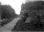 Två män sitter vid ett järnvägsspår som går mellan två branta bergväggar.