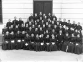 Konfirmandgrupp, sannolikt vid läroverkets entré i Enköping, 1897. Präst sannolikt komminister Walter Gustafsson (1856-1931).
