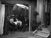Två kvinnor och två män vid kaffebord utanför ett hus