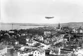 Vy från Stadsparken i Jönköping med Zeppelinare i luften, med reklam för Sidenhuset på Östra Storgatan. (Troligen fotomontage).