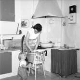 En husmor står i sitt kök och tvättar i en tvättbalja för hand den 4 november 1957.