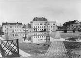 Östra torget i Jönköping med stora regnpölar på kullerstenen. Några människor står i grupper och samtalar med varandra.