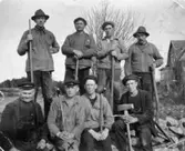 Åtta män med hackor och spadar vid bygget av Rygatan i Mölndal. Undre raden, andra från vänster står Oscar Lindberg. Okänt årtal.