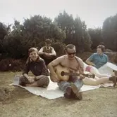 En man sitter och spelar gitarr på en gräsmatta. Elever från Streteredshemmet, på utflykt under 1970-talet.