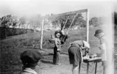 Bosgårdens barnträdgård 1938-1945. Fem barn vid en gungställning. Ett av barnen gungar, två av dem målar vid ett bord.
