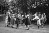 Midsommarfirande på Kvarnbygatan 23, 1920-tal. 
Den stora flickan längst till vänster är Astrid Andersson. Barnen i främre raden är: nr 2 från vänster Lisa Malmberg (i sjömansmössa), nr 5 är Margot Fässberg (g. Dalkvist), nr 6 är Pelle Malmberg (ljust klädd, brett bälte). Ovanför och något till vänster om Pelle Malmbergs huvud ses Tyra Johansson (t v) och Annika Lövberg (t h). (Lisa Malmberg föddes 1917).