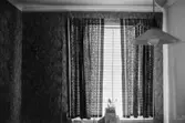 Bostadshus Roten M 11-12, okänt årtal. Ett rum med en tapetserad vägg, lampa och gardiner.
