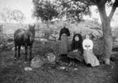 Bakre raden från vänster står en häst, Maria Eriksson och Anna Carlsson vid Vommedal Östergård 1907 - 1910. Framför dem sitter Valdeborg Johansson och Josefina 