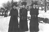 Tre damer med pälsmuffar och stora hattar på vinterpromenad.
I början av 1900-talet.