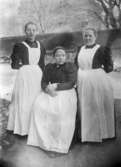 Sköterskorna Anna Ahlberg, Hanna Johansson samt kokerskan Mari Johansson utanför Mölndals sjukstuga år 1895.