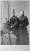Tre kvinnor uppställda i en fotoateljé år 1900. Amalia Precht-Reuter (1871-1956) står i mitten. Hon var dotter till sockerbruksmästaren Precht-Reuter vid Korndals bruk, senare anställd vid Carnegies bruk.