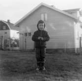 En pojke står på en gräsmatta framför villorna på Klevgatan 3 och 2. 1960-tal.