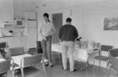 Dokumentation av Sagåsens flyktingförläggning 1992. Två personer som står ett kök möblerat med bord och stolar.