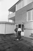 Dokumentation av Sagåsens flyktingförläggning 1992. Två personer står utanför en öppen entrédörr in till en byggnad. I bakgrunden syns ett insynsskydd.