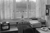 Dokumentation av Sagåsens flyktingförläggning 1992. Del av ett kontorsrum med tv, telefon, skrivare och fax. I fönstret står en krukväxt.