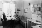 Arbetarbostad som troligtvis tillhör Krokslätts fabriker. Köket med de boende vid köksbordet.