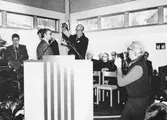 Jon E. Lisshammar fotograferar pastor Holger Sjögreen vid invigningen av Pingstkyrkan i Kållered söndagen den 1/3 1981. Från vänster är Sällskapet Länkarnas ordförande Erik Jörneborn som överlämnar ett silverkors. Den längst t.v är Gösta Gunnarsson. I talarstolen ses Erik Jörneborn och pingstpastor Holger Sjögreen. Till höger om Sjögreen ses pingstpastor Paul Åsberg, en okänd, pastor L. Larsson från Missionskyrkan i Kållered, Ansvarsavdelningschef Harry Lundgren, chefredaktör.