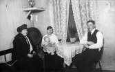 Familjen Karlsson sitter i köket på Kvarnfallet 31, år 1922. Från vänster: okänd dam, Alma Karlsson med dottern Astrid i knät och Viktor Karlsson.