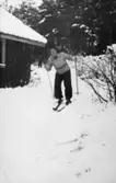 Astrid Garthman åker skidor förbi ett litet hus i Fjärås, 1930- 40-tal.